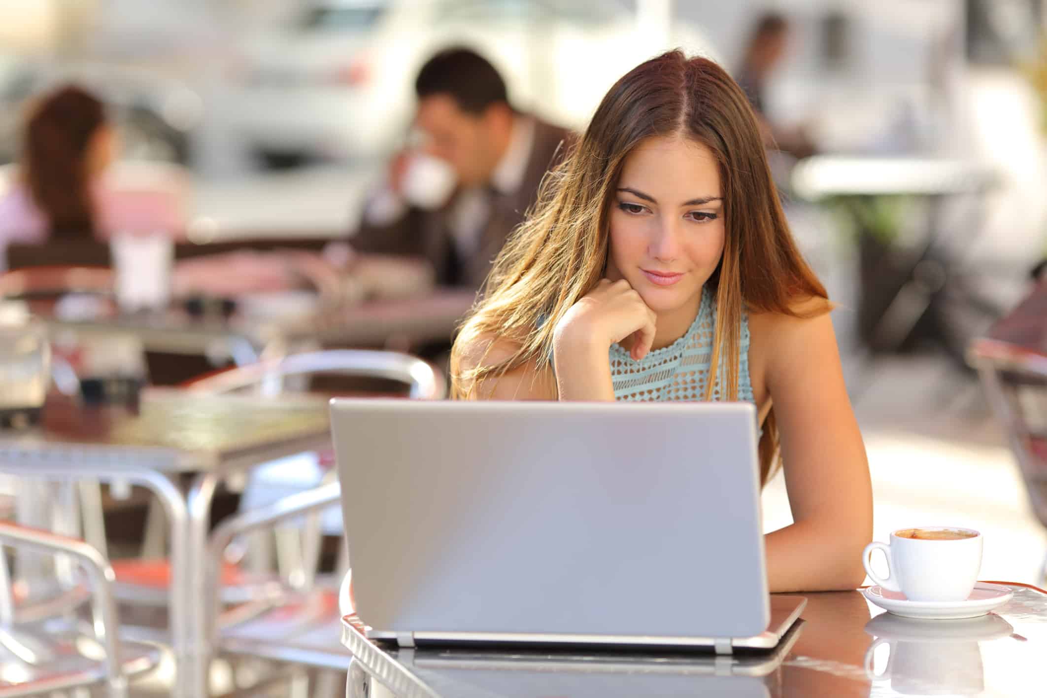 Woman watching laptop at an outdoor café, representing engagement with whiteboard animation videos and their psychology.