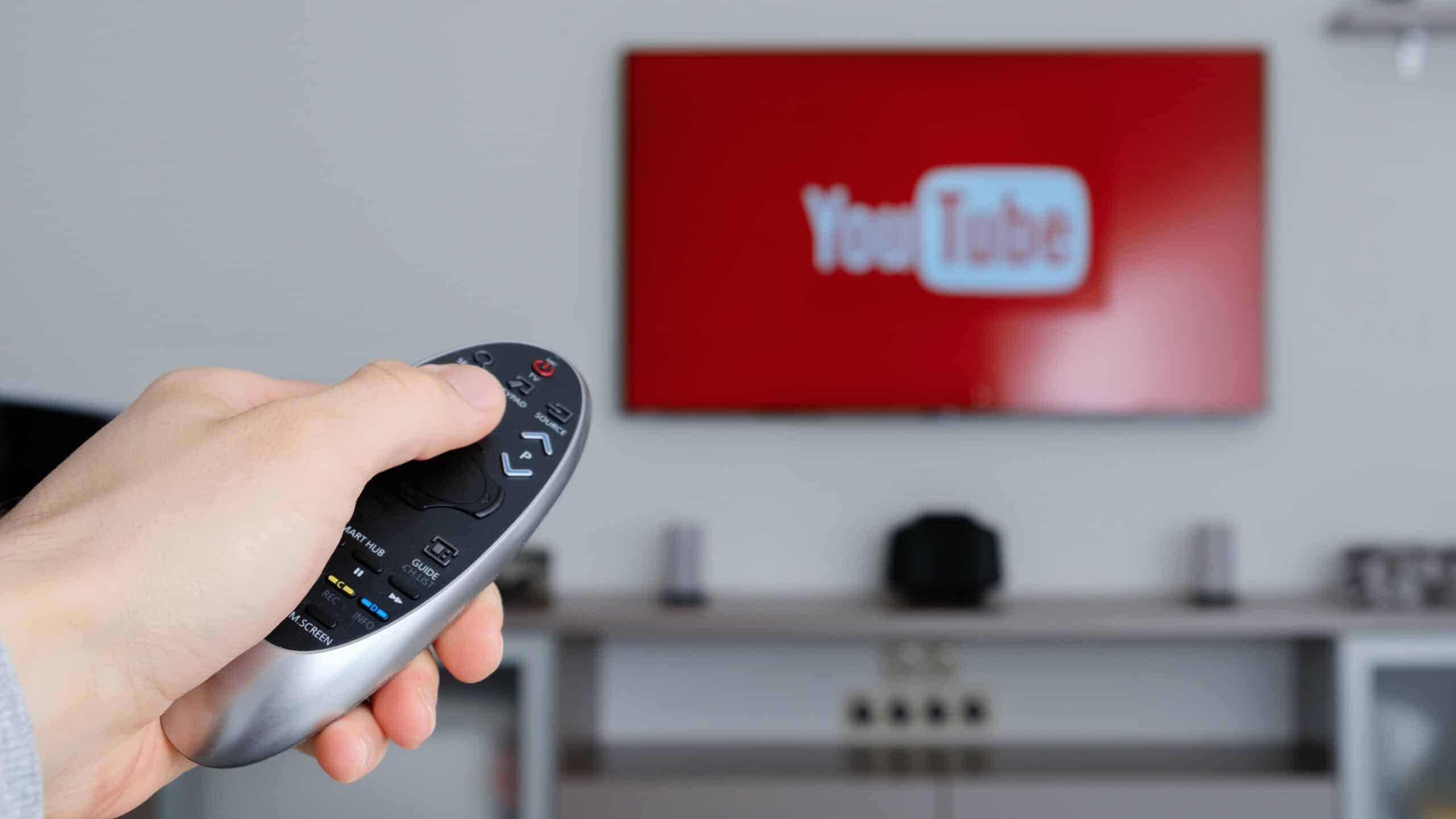 Hand holding a remote pointed at a TV screen displaying the YouTube logo, representing video marketing strategies.