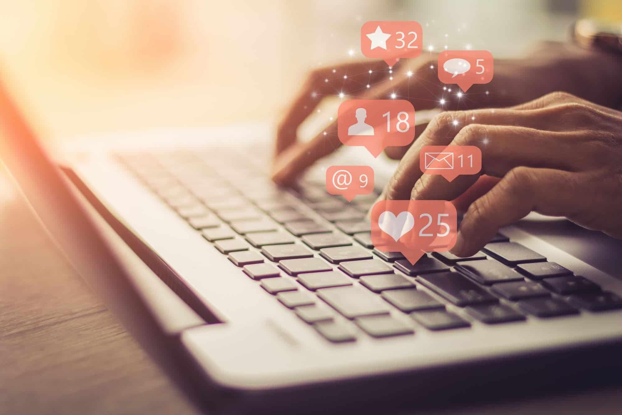 Hands typing on a laptop with social media icons floating, symbolizing engagement for effective marketing videos.