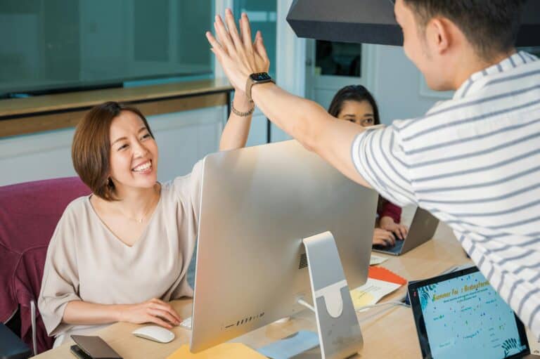 Smiling colleagues celebrate with a high-five at a desk, symbolizing teamwork and the success of Whiteboard Videos.