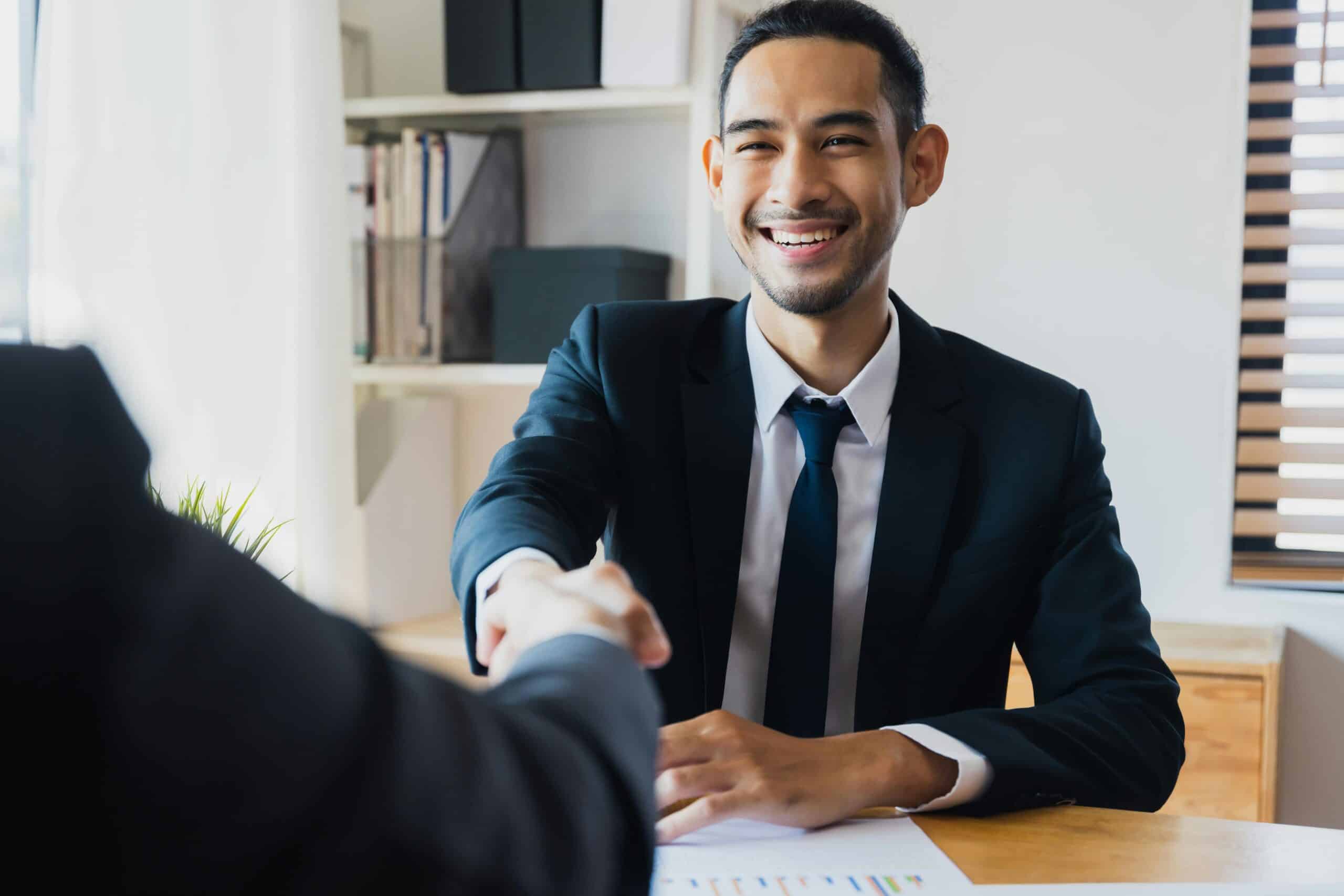 Smiling businessman in a suit shaking hands, symbolizing authenticity and trust in building strong relationships.