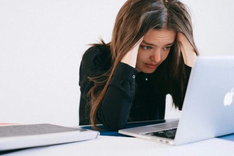 Stressed woman holding her head while looking at a laptop, frustrated by poor work results.