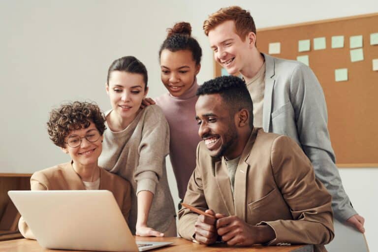 A group of coworkers smiling and engaged while watching a training video on a laptop in an office setting.